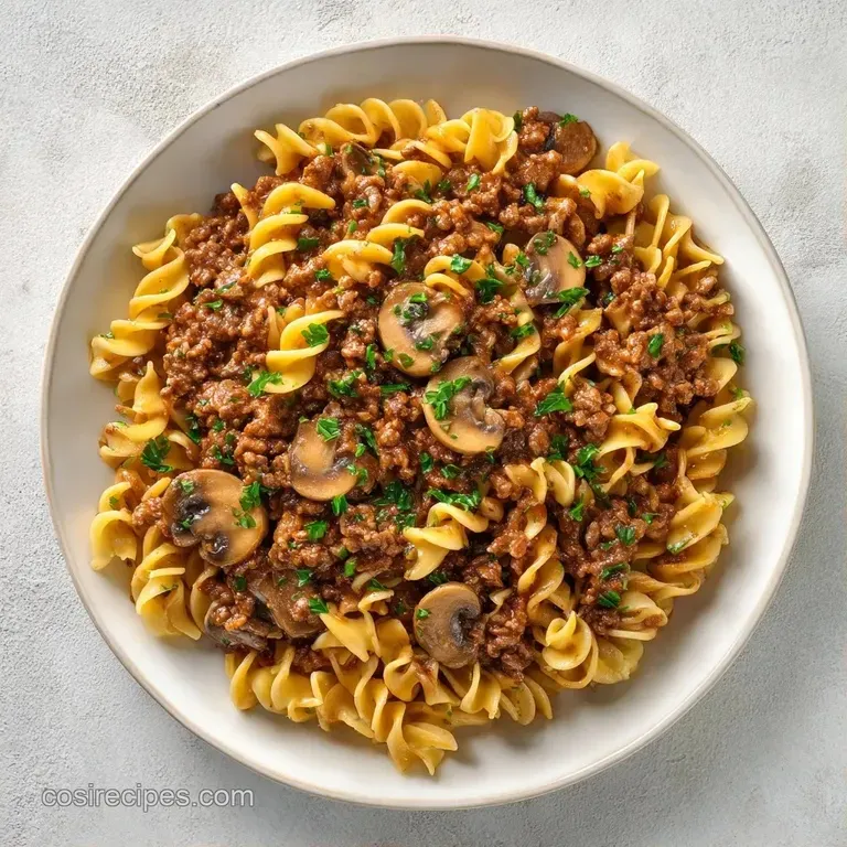 A shallow white bowl of rich, creamy meat sauce and mushrooms atop swirled noodles, garnished with bright green herbs.